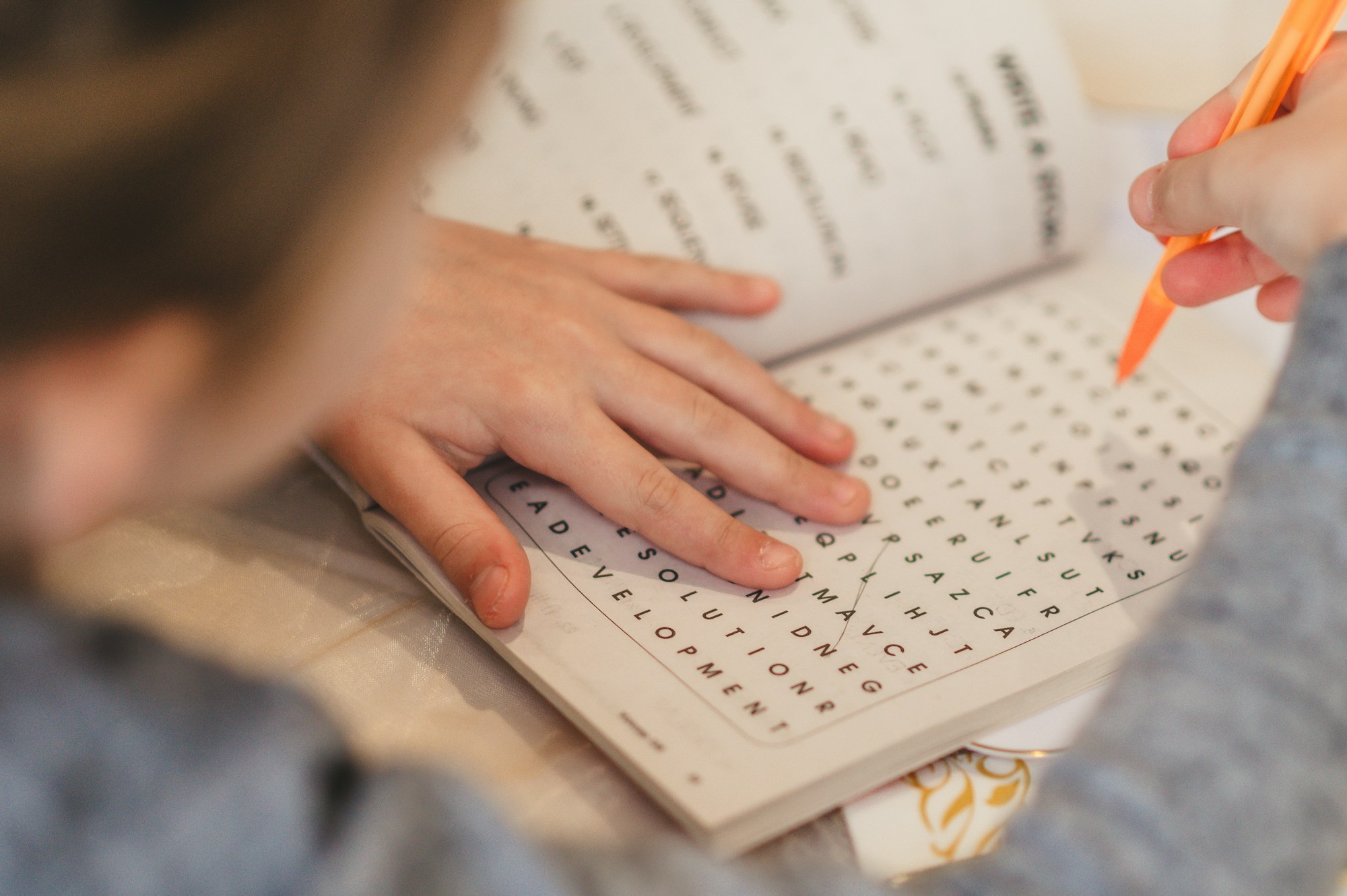Hands working a word search with an orange pen